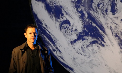 Luke Jerram standing in front of a projection of Earth