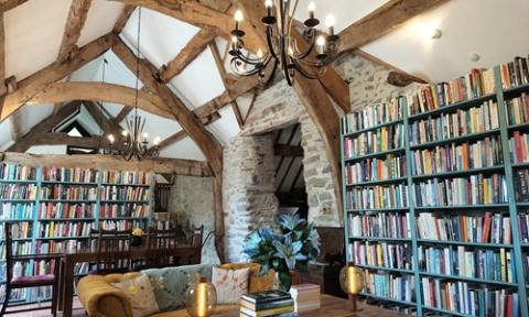 3.	A large room with a wooden-beamed high ceiling, lined with bookshelves and including several sofa, chairs and writing desks