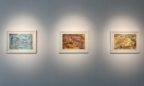 A curated trio of abstract framed paintings, each spotlighted to enhance its unique palette—cool blue and green swirls, vibrant red and purple tones, and warm yellow and brown hues