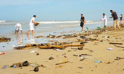 Group of people cleaning up plastic waste and rubbish from a beach.