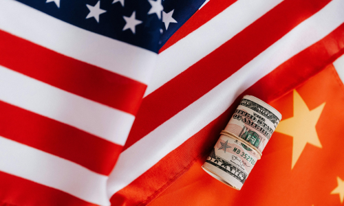 The American and China flag draped over each other, with a roll of dollars on top 