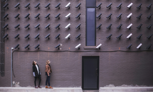 A wall of cctv camera mounted on a wall, looking down with two woman looking up