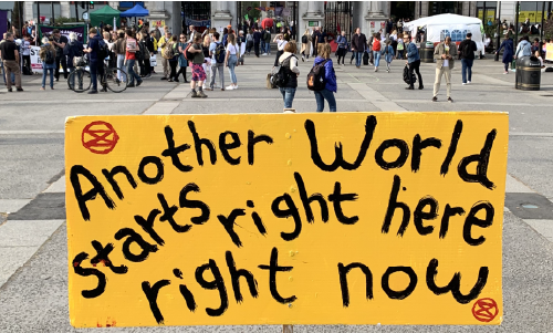 Extinction Rebellion protest in London; in foreground - placard reading Another World starts right here right now.