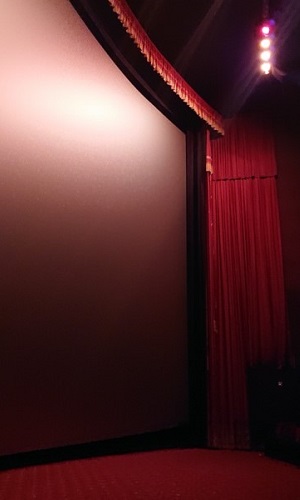 a photograph showing a section of the enormous IMAX screen in the auditorium at the Chinese Theatre in LA. The screen is framed around its edge by red velvet curtains and trim.