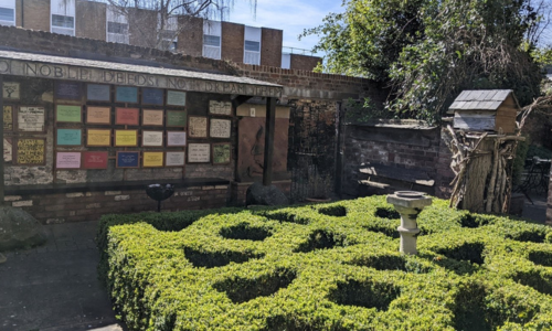  Image of a garden with a series of memorial plaques to local heroism behind it. Above the plaques, a board reads these words: Do noble deeds not dream them. The location is the garden of Octavia Hill Birthplace Museum.