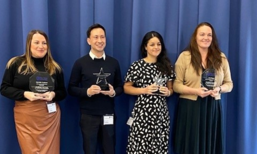 Four students, three female and one male, holding trophies and looking off-camera