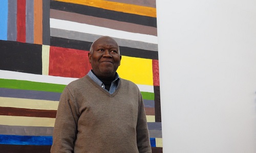 Dr Atta Kwami stood in front of a stripy painting