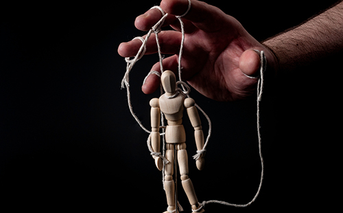 Hand controlling a wooden puppet on strings