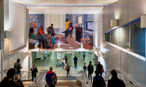 Commuters walk down steps in Brixton underground station while a large painting hangs above them.