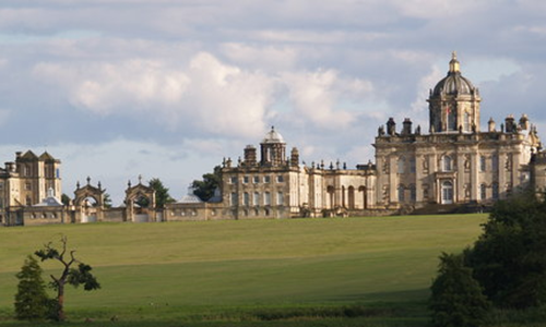 View of Castle Howard exterior north front, main house crowned by a dome, with west wing and separate kitchen block, in a grassy landscape.