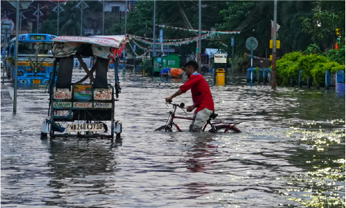 A man wearing a red top attempting to cycle a bike through knee high flooding