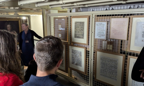 A group of people looking at framed paintings in the storage area of a museum.