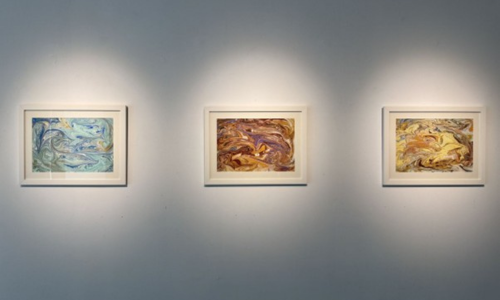 A curated trio of abstract framed paintings, each spotlighted to enhance its unique palette—cool blue and green swirls, vibrant red and purple tones, and warm yellow and brown hues