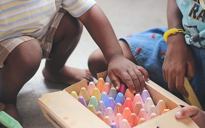 Photo by Tina Floersch on Unsplash - image shows the hands of two small children reaching into a colourful box of chunky chalks