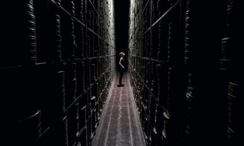 A woman stood in a darken hallway of stacked movie reel containers.