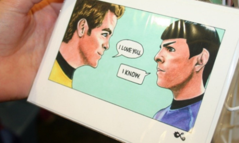 Hand holding an image of two men, one saying ‘I love you’, the other ‘I know’.