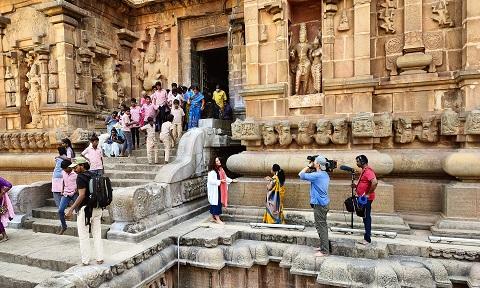 presenter Bettany Hughes is filmed by a camera crew in front of a temple in India with tourists in the background