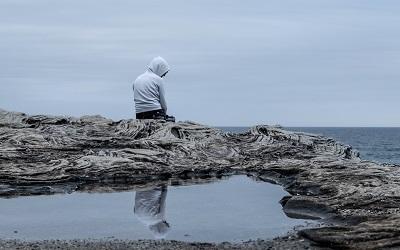 Young male sits on the edge of a rock on a beach looking deep in thought