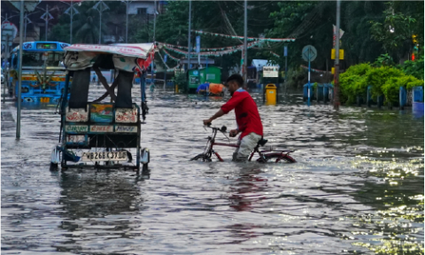 A man wearing a red top attempting to cycle a bike through knee high flooding