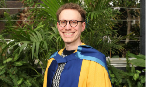 Daniel Tammet smiles proudly wearing Open University academic dress