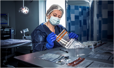 A female forensics scientist wearing protective clothing removes two test tubes from a transparent evidence bag at a workstation in a laboratory
