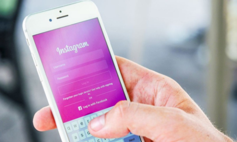 A hand holds a mobile phone showing the ‘Instagram’ homepage