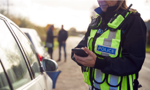 Police woman inputting information into a ticket machine standing next to a car