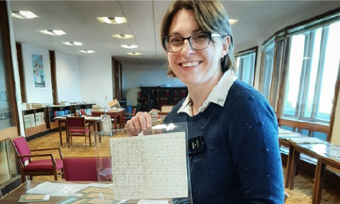 Professor Rosalind Crone holds up a handwritten document to the camera in an Archive