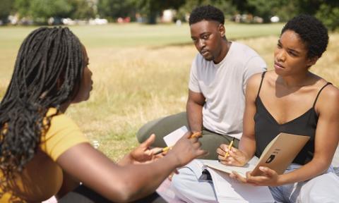 Three Minority Ethnic students sitting on grass talking to each other