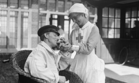 A member of the Voluntary Aid Detachment (VAD) lighting the cigarette of one of her convalescent patients at the Royal Naval Hospital, Chatham during the First World War.