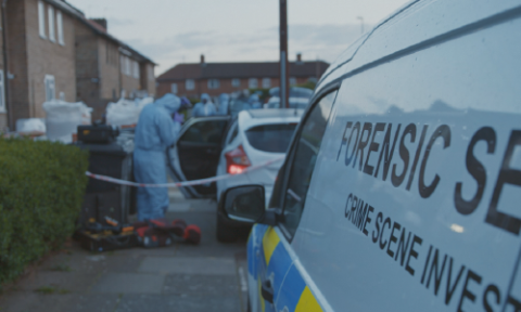 Police forensic experts examine a crime scene, with a white car taped off on a suburban street, and the Crime Scene Investigation team’s white van in the foreground