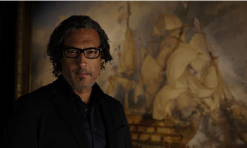 Presenter Historian David Olusoga against a backdrop of a dramatic nineteenth century oil painting of a naval battle