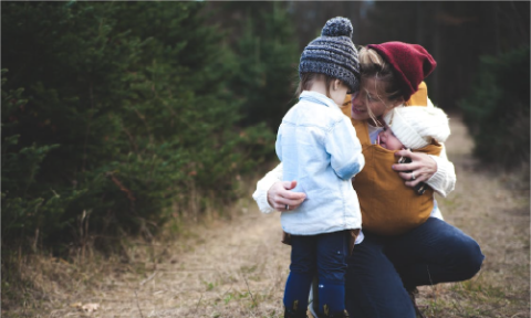 Woman with brown baby carrier and little kid in white jacket